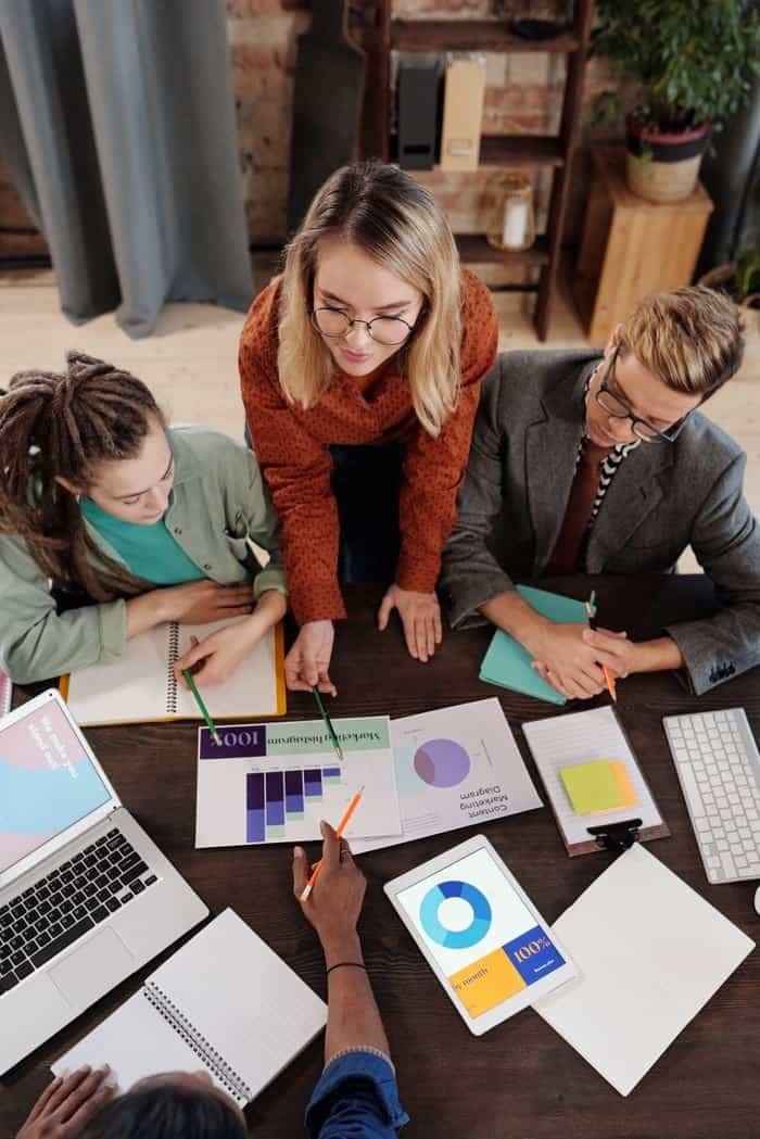 Home Top view of a diverse group discussing business reports and charts around a desk.